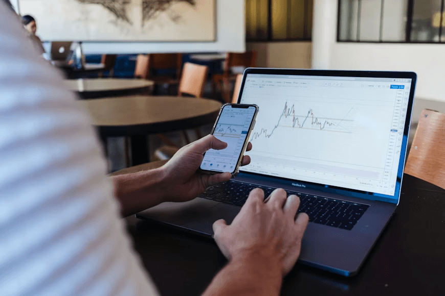 Man examining cryptocurrency data on phone with laptop